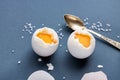 Hard-boiled eggs on a blue pastel background, half peeled, next to it are shells, salt and a spoon. The concept of a
