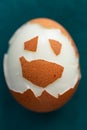 Hard-boiled half unshelled chicken egg on green background. Funny face made of eggshell on the surface.