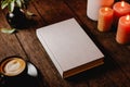 Hard cover book mock up on wooden table. Night interior with candles, plant and coffee. 3D rendering