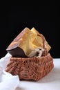 Hard craft cheese in a brown wicker basket. Chunks of hard cheese on a black background. Vertical photo Royalty Free Stock Photo