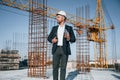In hard hat, holding plan in hands. Businessman in formal clothes is on the construction site at daytime Royalty Free Stock Photo