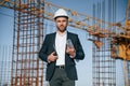 In hard hat, holding plan in hands. Businessman in formal clothes is on the construction site at daytime Royalty Free Stock Photo