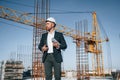 In hard hat, holding plan in hands. Businessman in formal clothes is on the construction site at daytime Royalty Free Stock Photo