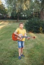 Hard of hearing preteen boy playing guitar outdoors. Child with hearing aids in ears playing music and singing song in park. Hobby