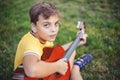 Hard of hearing preteen boy playing guitar outdoors. Child with hearing aids in ears playing music and singing song in park. Hobby