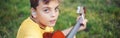 Hard of hearing preteen boy playing guitar outdoors. Child with hearing aids in ears playing music and singing song in park. Hobby