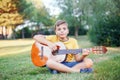 Hard of hearing preteen boy playing guitar outdoors. Child with hearing aids in ears playing music and singing song in park. Hobby