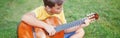 Hard of hearing preteen boy playing guitar outdoors. Child with hearing aids in ears playing music and singing song in park. Hobby