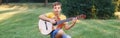 Hard of hearing preteen boy playing guitar outdoors. Child with hearing aids in ears playing music and singing song in park. Hobby