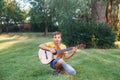 Hard of hearing preteen boy playing guitar outdoor. Child with hearing aids in ears playing music and singing song in park. Hobby