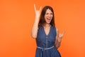Hard rock lover. Delighted crazy brunette woman in denim dress making devil horns gesture with fingers up Royalty Free Stock Photo
