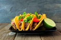 Hard shelled tacos with ground beef, vegetables and cheese on a dark background