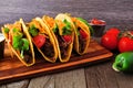 Hard shelled tacos with ground beef, vegetables and cheese, scene with wood background