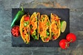 Hard shelled tacos with ground beef, vegetables and cheese, top view on a dark background