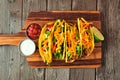 Hard shelled tacos with ground beef, vegetables and cheese, top view on a wood background