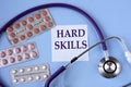 HARD SKILLS - words on a white piece of paper on a blue background. A stethoscope and pills lie side by side