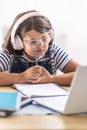 Hard-studying girl in glasses wears headphones and chews on pencil in her hand looking into the pc Royalty Free Stock Photo