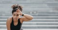 Hard training and rest. Tired woman with headphones and fitness tracker wipes sweat from forehead