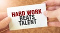 HARD WORK BEATS TALENT word inscription on white card paper sheet in hands of a businessman