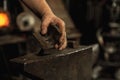 Close-up working powerful hands of male blacksmith forge an iron product in a blacksmith. Hammer, red hot metal and Royalty Free Stock Photo