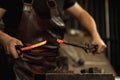 Close-up working powerful hands of male blacksmith forge an iron product in a blacksmith. Hammer, red hot metal and