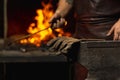 Close-up working powerful hands of male blacksmith forge an iron product in a blacksmith. Hammer, red hot metal and Royalty Free Stock Photo