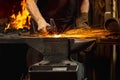 Close-up working powerful hands of male blacksmith forge an iron product in a blacksmith. Hammer, red hot metal and Royalty Free Stock Photo