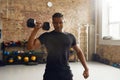 Hard Worker. Young athletic man looking at camera, lifting dumbbell while having workout at industrial gym. Sport Royalty Free Stock Photo