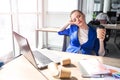 Hard-working woman is sitting at the table and has some rest. She is bored and tired. Woman has a cup of coffee in her