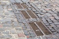 Hardscape sett road with iron grate of the drainage system hatch.