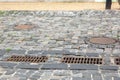 Hardscape sett road with iron grate of the drainage system hatch.