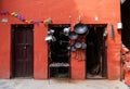 Hardware store with metal goods - pans, sickles, hoes, tools, tableware hinged on a terracotta shop wall. Narrow Nepalese street