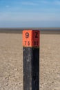 Hardwood pole with an orange head and a painted mark on an empty beach at the Dutch North Sea