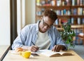 Hardworking black man writing down info from textbook, getting ready for test at cafe