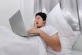 Hardworking people concept. Tired overworked young Asian man sleeping with computer laptop on the bed in bedroom Royalty Free Stock Photo