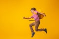 Hardworking schoolboy in uniform with a backpack runs on a yellow background