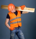 Hardy labourer concept. Man in helmet, hard hat and protective gloves holds wooden beam, grey background. Carpenter