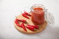 Harissa in a glass jar on a wooden stand and hot chili peppers on a white background Royalty Free Stock Photo