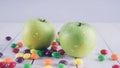 Apples and candies on a white wooden table. Harmful and healthy food on a white background.