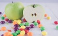 Apples and candies on a white wooden table. Harmful and healthy food on a white background.