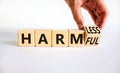 From harmful to harmless. Businessman turns the wooden cube and changes word harmful to harmless. Beautiful white table, white