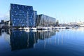 Harpa Concert Hall reflected in calm water of Reykjavik Harbor on sunny morning.