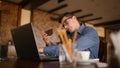 Harried handsome young businessman in glasses working on laptop, talking on phone, taking notes and searches info in