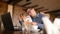 Harried handsome young businessman in glasses working on laptop, talking on phone, taking notes and searches info in