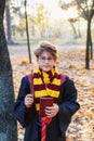 Harry Potter boy in glasses stands in autumn park with gold leaves, holds book in his hands