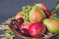 Harvest of autumn fruits in a wooden plate. Composition with autumn yellow leaves on black background. Royalty Free Stock Photo