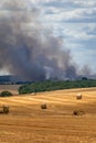 Harvested field with straw bales in summer on a sunny day with a field fire and smoke in the background