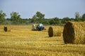 Harvested wheat field with large round bales of straw in summer. Tractor forming bales is visible background. Farmland Royalty Free Stock Photo