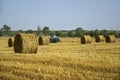 Harvested wheat field with large round bales of straw in summer. Tractor forming bales is visible background. Farmland Royalty Free Stock Photo