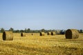 Harvested wheat field with large round bales of straw in summer. Tractor forming bales is visible background. Farmland Royalty Free Stock Photo